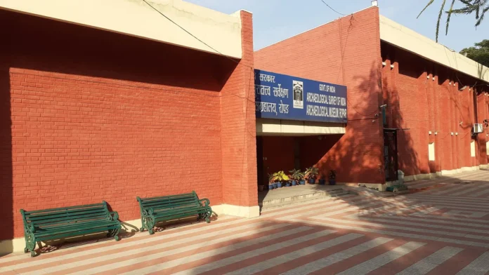 Red brick entrance of the Archaeological Survey of India museum in Ropar, with a blue sign board and two green benches
