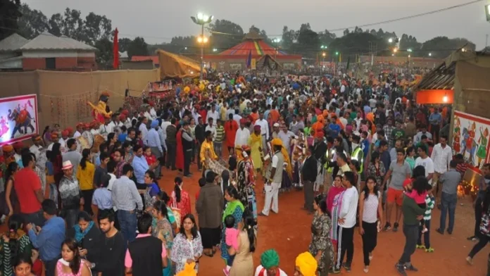 Evening crowd walking between craft stalls and a striped tent at the Chandigarh National Crafts Mela, Kalagram