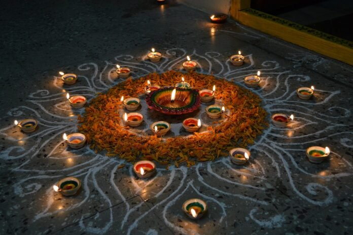 Lit clay diyas arranged around marigold petals and a white rangoli pattern on a floor during the festival season