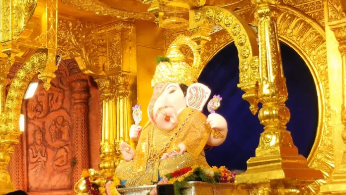 Idol of Dagadusheth Halwai Ganapati in Pune seated under a carved golden canopy, decorated with flower garlands
