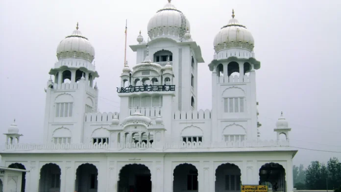 White Gurdwara Patalpuri Sahib at Kiratpur Sahib with three domed towers and a row of arches, on a hazy day