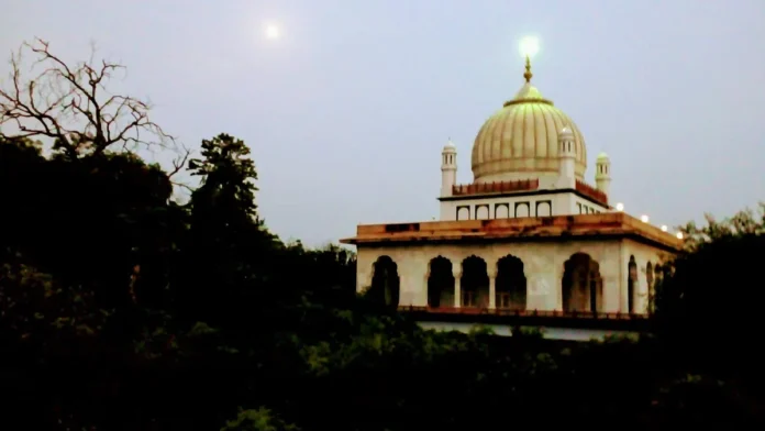 Domed tomb of Shaikh Ahmad Sirhindi at Rauza Sharif, Sirhind, above dark trees at dusk, with the moon in the sky