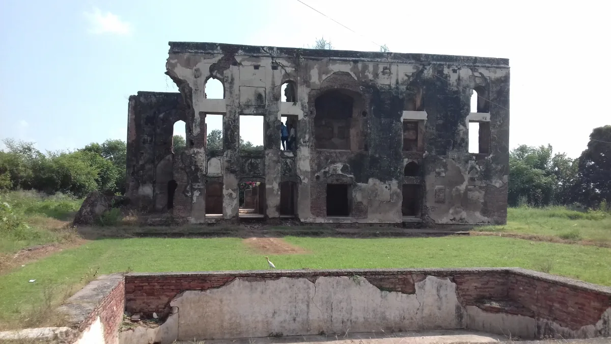 Two-storey ruined brick palace with empty arched openings and peeling plaster behind a lawn and a low tank wall at Aam Khas Bagh, Sirhind