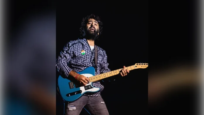 Arijit Singh playing a blue electric guitar on stage at a 2023 concert