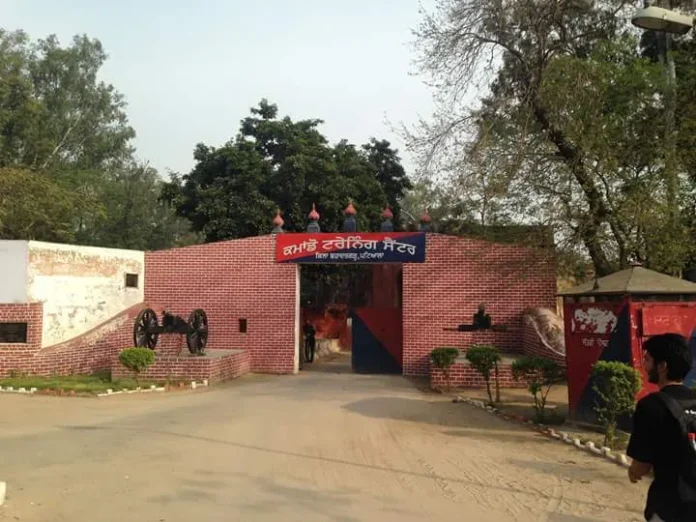 Red brick gateway at Bahadurgarh Fort with two old cannons, a red and blue sign in Punjabi reading Commando Training Centre and a visitor walking past on the right