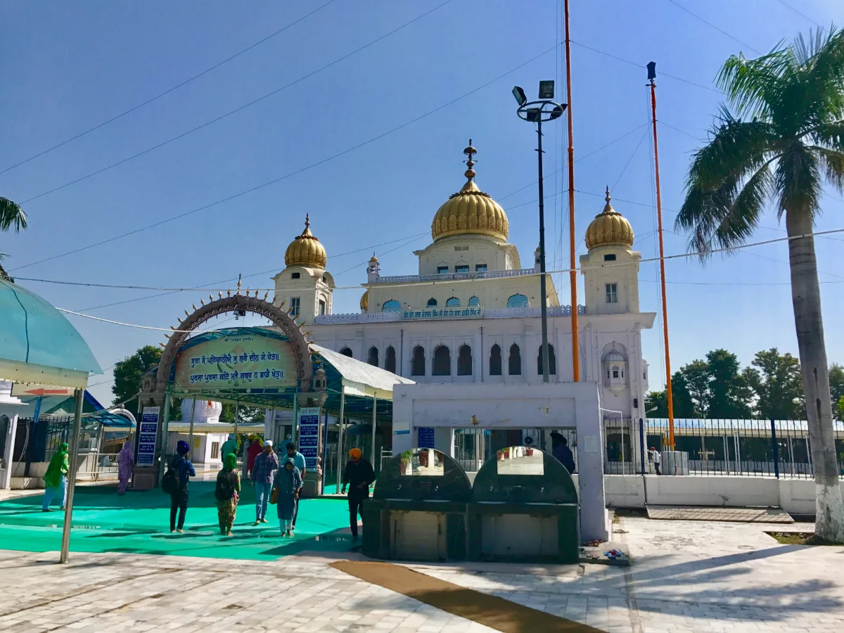 White gurdwara with golden domes behind an arched entrance canopy at Gurdwara Fatehgarh Sahib, Sirhind, with devotees crossing the courtyard