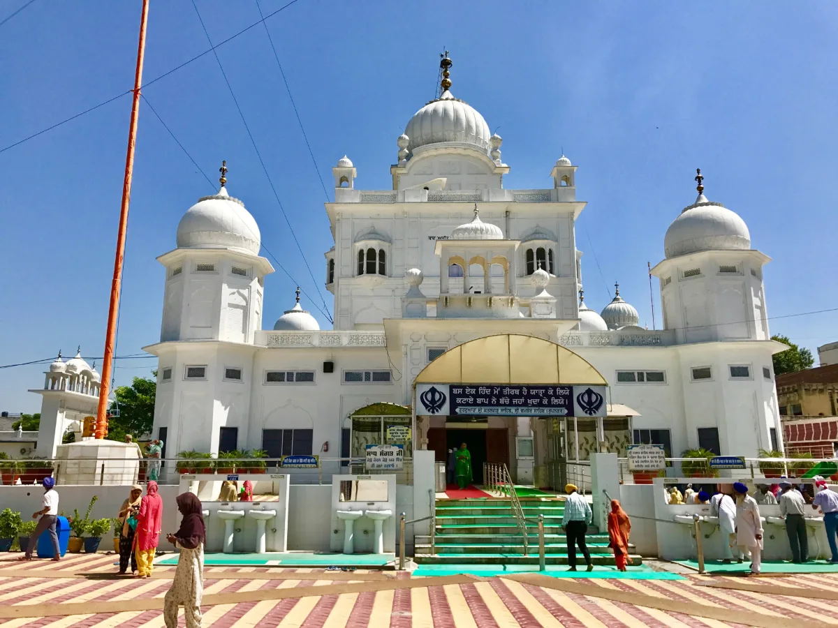 White domed Gurdwara Katalgarh Sahib at Chamkaur Sahib under a blue sky, with wash basins in front and devotees walking on a patterned courtyard