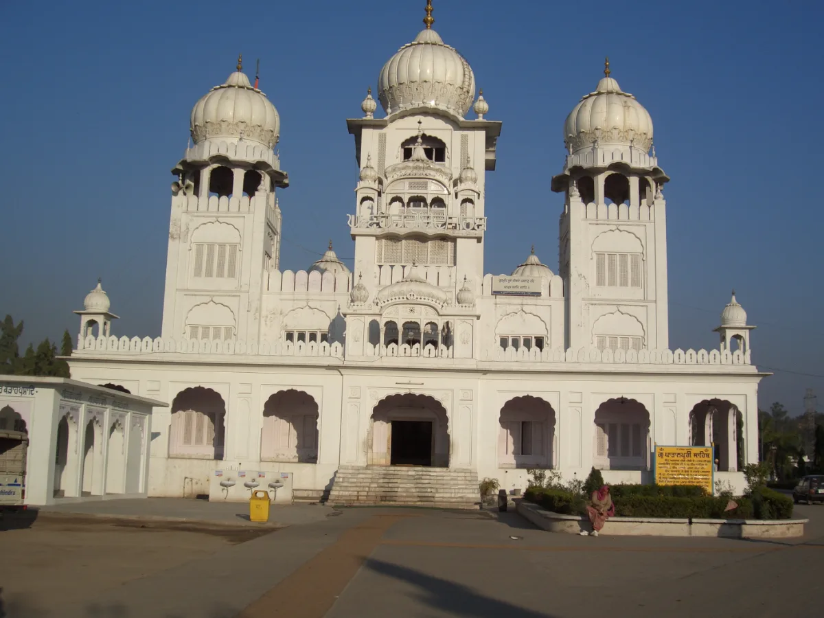 White multi-domed Gurdwara Patalpuri Sahib at Kiratpur Sahib, with three domed towers, an arched entrance and a low hedge in front
