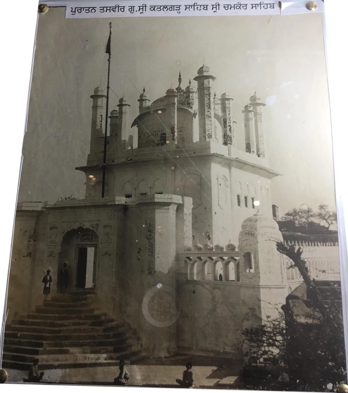 Old sepia photograph of the earlier Gurdwara Katalgarh Sahib at Chamkaur with a flag pole, a flight of steps and small domed turrets