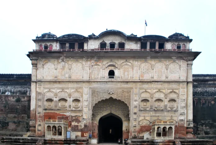 Weathered pale main gate of Qila Mubarak in Patiala with a carved arched entrance, rows of niches, small balconies and a flag on the roof