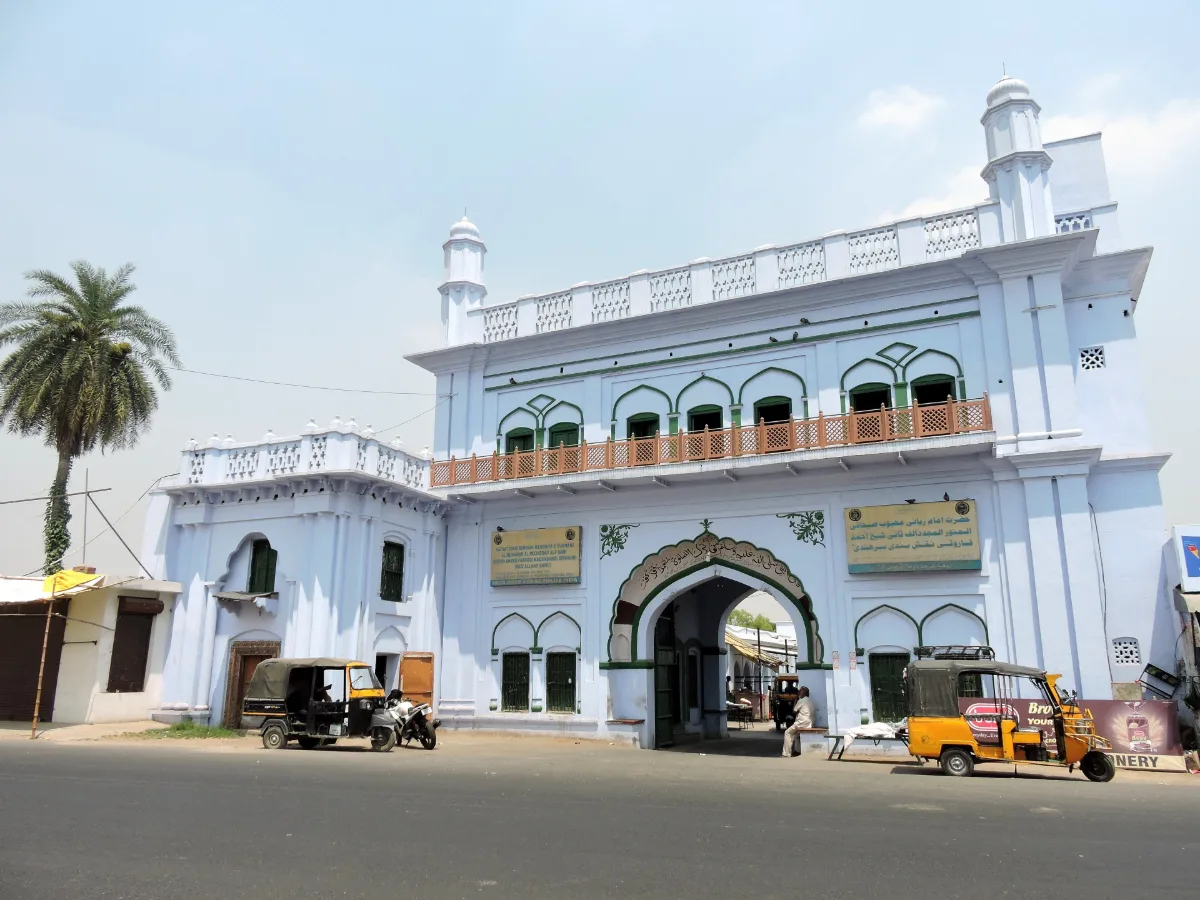 Pale blue entrance building of Rauza Sharif at Sirhind with a pointed arch gateway, green-arched windows and a balcony, seen from the road